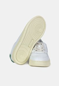 Sneaker bianche in pelle con design perforato, lacci beige e suola in gomma leggera beige texturizzata; accent verde sul tallone.
