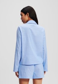Compleu din țesătură împletită de culoare albastru deschis, format dintr-o cămașă cu mânecă lungă și guler, împreună cu pantaloni scurți asortați, având o textură fină și o croială lejeră.