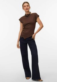 Haut marron ajusté avec des manches courtes, ourlet asymétrique, associé à un jean évasé bleu foncé et des sandales noires.