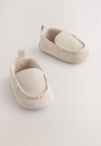 Chaussures bébé beige en daim, faciles à enfiler, avec une texture douce, un détail de surpiqûre autour de l'ouverture et une petite languette à talon pour un enfilage facile.