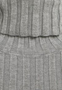Gros plan sur un tissu tricoté côtelé gris avec des rayures texturées verticales et des couches pliées, mettant en valeur le motif textile et les détails de couture.