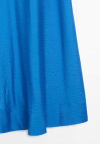 Blue textured fabric with slight sheen and natural folds hanging freely against a white background.