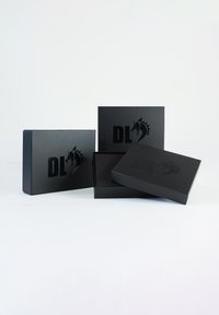 Zwarte cadeau-dozen met matte afwerking, met de letters "DL" en een paardenlogo verdiept op de bovenkant. Eén doos is iets open waardoor de binnenkant zichtbaar is.