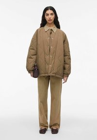 Vadderad brun jacka med hög krage och tryckknappar, i kombination med matchande beige kordbyxor och mörkbruna slip-on skor.
