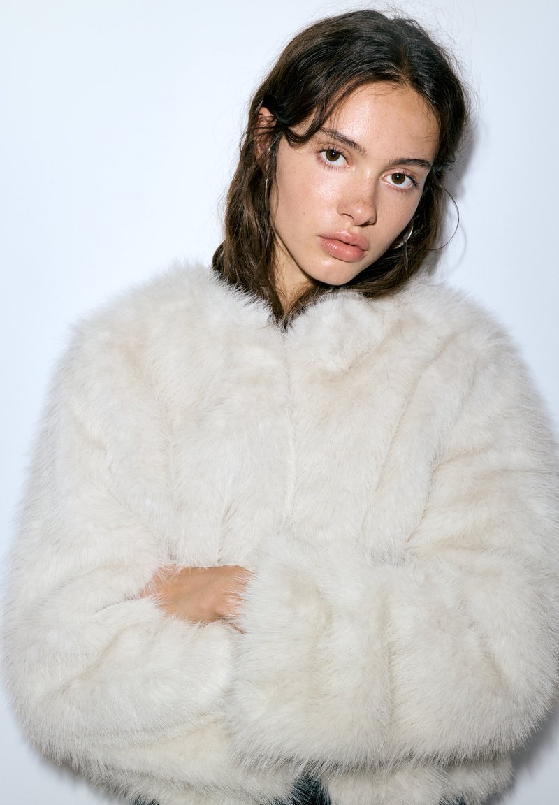 Hvid jakke i imiteret pels med en blød og fyldig struktur, korte ærmer og rund halsudskæring, prydet med bløde, fnuggede detaljer over det hele.