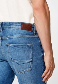 Ljusblå denimjeans med ett lädermärke på midjebandet. Har två bakfickor och en rak bendesign.
