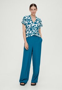 Bloemige blouse met korte mouw in wit en teal, gecombineerd met high-waisted, wijde teal broek. Soepele stof met een relaxte pasvorm.