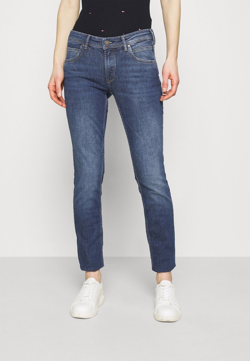 Slim-fit, mörkblå denimjeans med en mjuk textur, femfickorsdesign och kontrasterande sömmar. Bärs med vita sneakers.