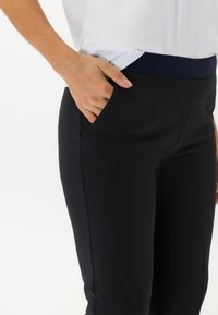 Zwarte broek met eenTailored fit en een gladde textuur. Beschikt over een contrasterende marineblauwe tailleband en zijzakken.