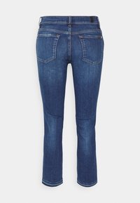 Tmavě modré džíny z denimu se zadními kapsami, poutky na opasek a viditelnými švy, zobrazené zezadu na bílém pozadí.