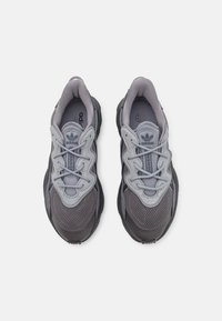 Šedé športové topánky s textilným vrchom, gumovou podrážkou a štruktúrovaným vzorom. Šnúrky v svetlošedej farbe a výrazné logo.