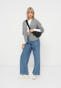 Grauer gestrickter Cardigan, weißes Crop-Top und weite blaue Jeans. Schwarze Umhängetasche und weiße Sneakers mit hellen Akzenten. Einfacher und moderner Look.