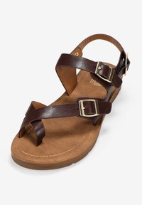 Sandal in pelle marrone con cinturini incrociati, due fibbie dorate e una soletta morbida color sabbia. Suola in gomma leggermente sollevata con dettagli di cucitura.