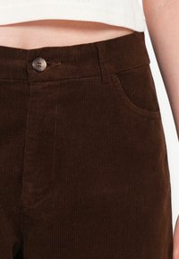 Bruine corduroy broek met ribbeltextuur, een sluiting met een knoop aan de voorkant en zijzakken voor praktisch gebruik.