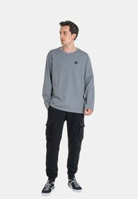 Gray long-sleeve shirt with a round neckline and a small black logo. Black cargo pants with pockets and black sneakers.