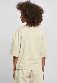 Béžové oversize bavlněné tričko s krátkým rukávem, kulatým výstřihem a hladkým povrchem. Minimalistický design bez viditelných vzorů nebo akcentů.