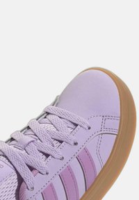 Fioletowe sneakersy z teksturowaną cholewką, płaskimi sznurowadłami i jasnobrązową gumową podeszwą. Posiadają trzy ciemniejsze fioletowe paski po bokach oraz przeszycia.