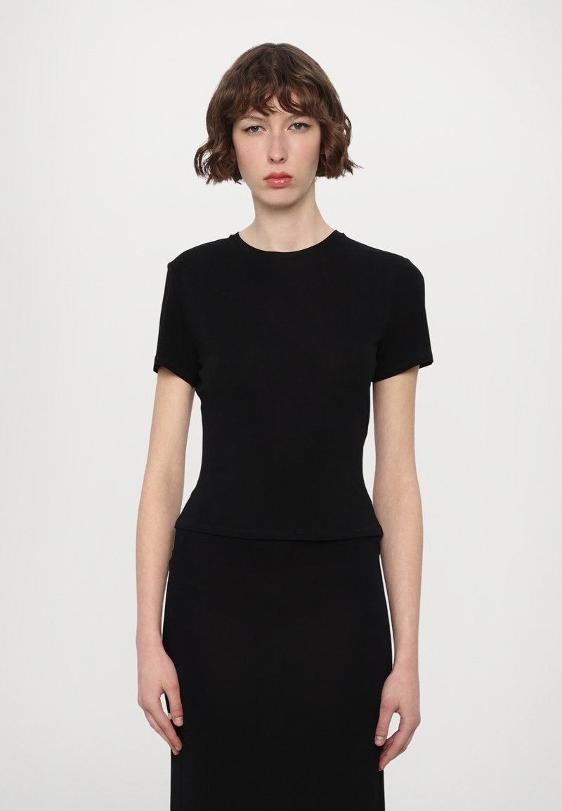 Black fitted T-shirt with short sleeves, round neck, smooth texture, designed for a close fit. Worn with a matching black skirt.