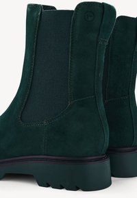 Bottes chevilles en suède vert avec panneaux latéraux élastiques, finition texturée et semelle extérieure épaisse et robuste. Des détails de couture renforcent le design.