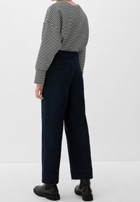 Suéter a rayas en blanco y negro con mangas sueltas, combinado con pantalones de mezclilla oscuros de tiro alto y pierna ancha, y botines negros hasta el tobillo.