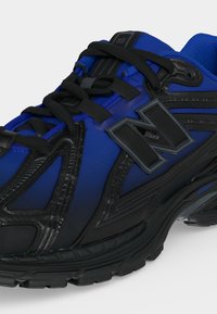 Baskets athlétiques bleues et noires avec une semelle épaisse, des lacets noirs et un grand logo « N » sur le côté.