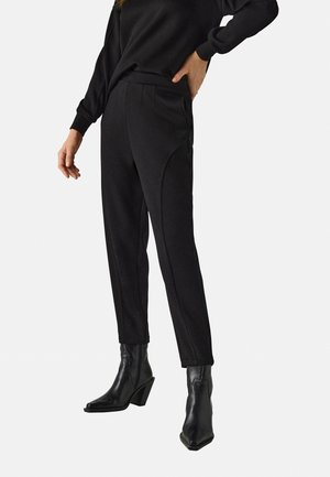 Pantalones negros ajustados con una textura suave, que cuentan con costuras laterales y una cintura de altura media, acompañados de elegantes botines negros hasta el tobillo.