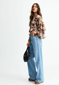Blommig, genomskinlig svart och beige blus med trumpetärmar, matchad med högmidjade, ljusblå utsvängda jeans och en liten svart handväska.