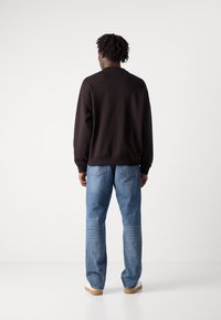 Sudadera negra con dobladillo acanalado, combinada con jeans de pierna recta azul claro y zapatos beige, vista desde la parte de atrás.