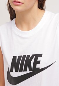 Vit ärmlös t-shirt i bomull med en stor svart Nike-logotyp över bröstet, rund halsringning och slät textur.