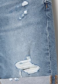 Light blue distressed denim shorts with frayed edges, featuring a large tear and rolled cuffs, highlighting texture and variations in fabric.