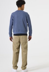 Sudadera azul con puños acanalados, logo en la parte posterior, combinada con pantalones de pana color caqui que tienen bolsillos laterales, usados con zapatillas blancas.