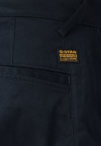 Temno modre denim hlače s prišeljenim G-Star Originals logotipom, vidnimi šivi in klasičnim dizajnom s petimi žepi. Gladka tekstura z natančno prileganje.