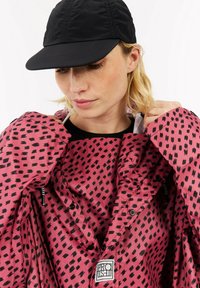 Rosa jakke med et sort abstrakt mønster, med knapper, et logo-patch og elastiske detaljer. Følger en sort kasket.