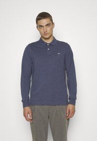 Navyblaues Langarm-Poloshirt mit Kragen, drei Knöpfen und einem kleinen Logo auf der linken Brust. Der Stoff wirkt weich und hat eine dezente Textur.