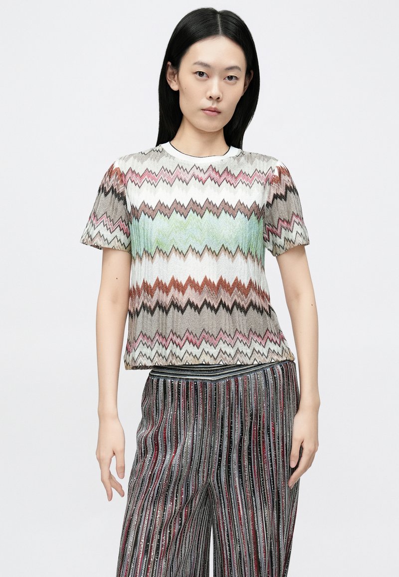 Multifarvet, zigzag-mønstret striktrøje med korte ærmer; blød tekstur og rund halsudskæring; kombineret med stribede bukser med vide ben.