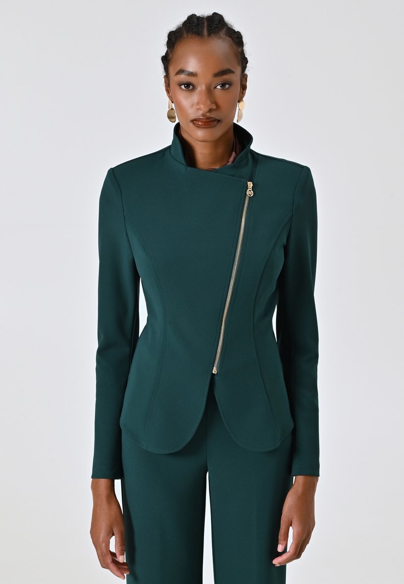 Groene, fitted blazer met hoge kraag, asymmetrische ritsluiting en gestructureerd ontwerp. Gemaakt van een soepele stof met minimalistische afwerking.