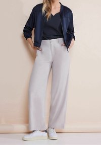 Námornícka bomber bunda, žebrovaný černý top a světle šedé kalhoty s širokými nohavicemi v kombinaci s bílými teniskami. Jednoduchý design s hladkými texturami.