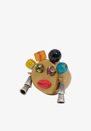 Anillo de oro con cuentas de colores que forman ojos, labios en esmalte rojo y borlas colgantes en tono plateado que asemejan pendientes.