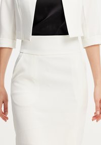 Blazer blanc ajusté à manches courtes et à la silhouette structurée, associé à une jupe crayon blanche moulante. Les deux sont sans coutures avec des accents minimaux.