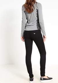 Šedý dlouhý rukáv top s krajkovými detaily na stranách, doplněný černými přiléhavými kalhotami a černými nazouvacími botami. Hladké textury a přiléhavý design.