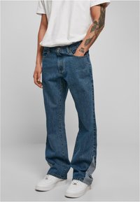 Blauwe denim jeans met een rechte snit, zichtbare stiksels en een lichte vervaging. Gecombineerd met witte sneakers en een eenvoudig wit T-shirt.