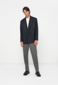 Navy pinstriped double-breasted blazer over a white t-shirt, paired with gray trousers and black chunky shoes. Simple, tailored design.