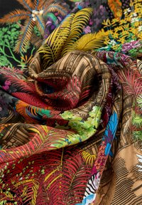 Tessuto colorato con motivi intricati della giungla in verdi, gialli, rossi e blu, che si drappeggia con un aspetto morbido e texture.