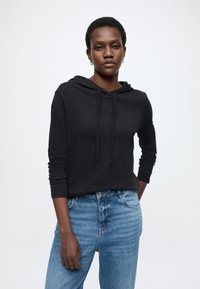 Μαύρο βαμβακερό φούτερ με μακριά μανίκια και κουκούλα με κορδόνι, σε συνδυασμό με ανοιχτόχρωμο τζιν παντελόνι. Ομαλή υφή, άνετη εφαρμογή.