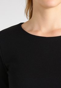 Svart stickad tröja med rund hals, figurnära design och slät yta. Tyget verkar mjukt och något stretchigt.