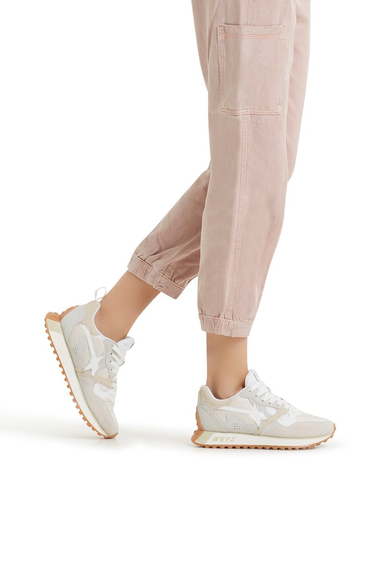 Sneakers di un beige chiaro con accenti bianchi, caratterizzati da una tomaia testurizzata, punta rotonda e una suola in gomma arancione resistente. Progettati per il massimo comfort.