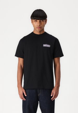 Black short-sleeve t-shirt made of cotton. Features a small rectangular logo patch on the left chest area. Straight cut.