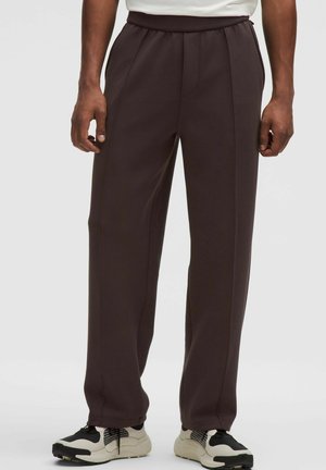 Braune, locker sitzende Hosen aus strukturiertem Material mit flachem Bund und Seitennähten. Getragen mit schwarz-weißen Sneakers.