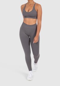 Szary stanik sportowy i pasujące legginsy z wysokim stanem wykonane z elastycznego, gładkiego materiału; noszone z białymi butami sportowymi.