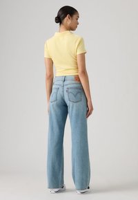 Κίτρινη ριγωτή πόλο μπλούζα συνδυασμένη με ανοιχτό μπλε τζιν παντελόνι με φαρδιά πόδια, με πίσω κορνίζα και δύο πίσω τσέπες. Απλός, καθημερινός σχεδιασμός.